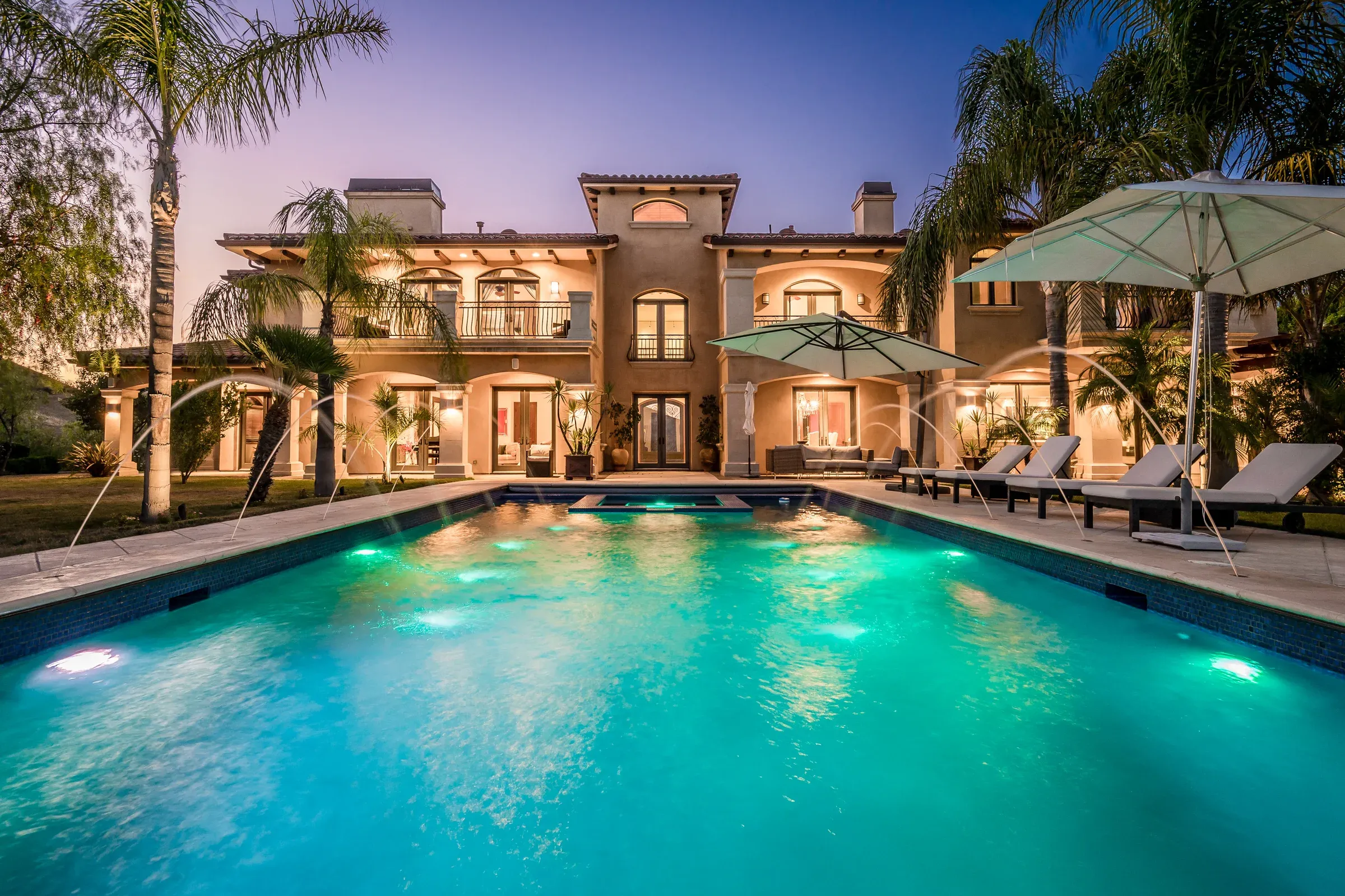 Beleuchteter Pool mit Steinumrandung vor einer Villa in der Dämmerung